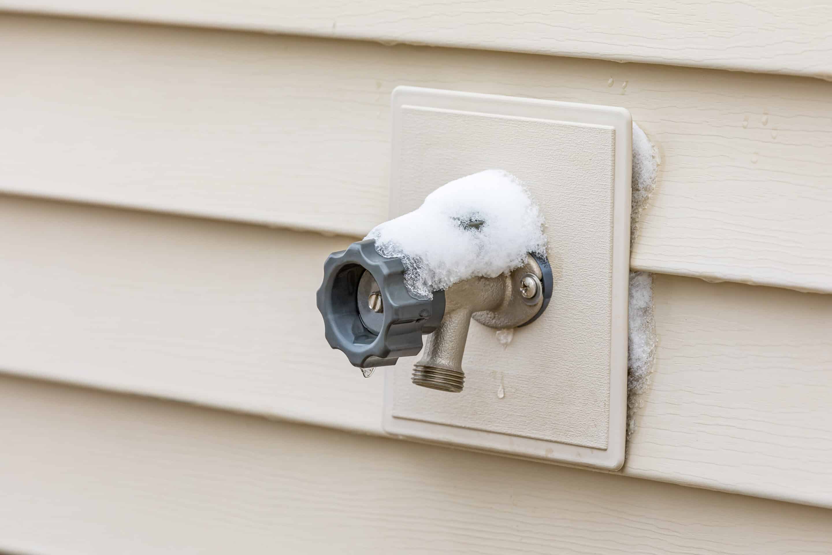 Outdoor faucet covered in snow during winter.